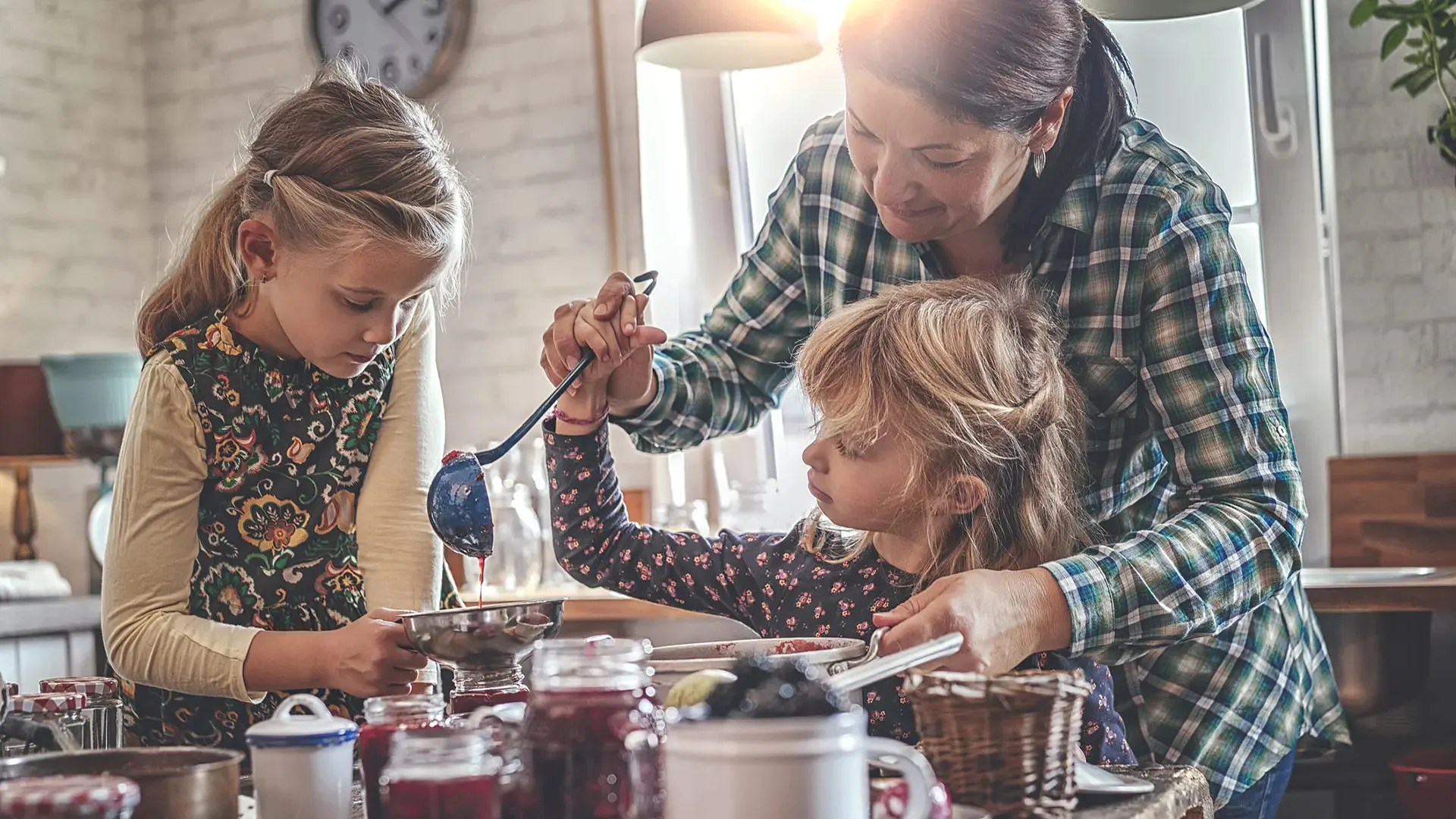 Une adulte et deux enfants préparent des confitures ensemble dans la cuisine
