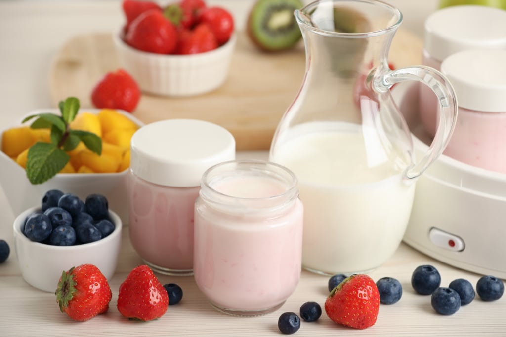Pots individuels pour yaourtière et différents fruits sur une table en bois blanc