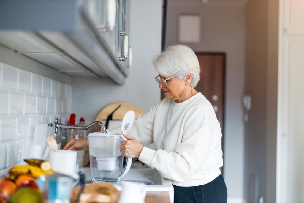Dame versant de l'eau dans sa carafe filtrante