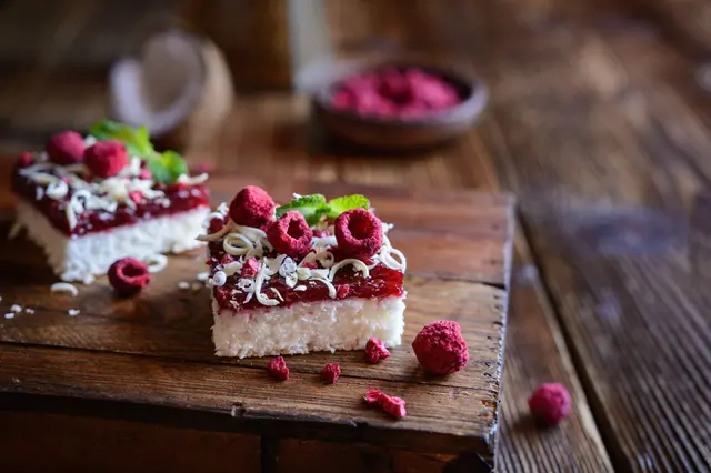 Gâteau à la noix de coco avec une couche de framboise, garni de copeaux de chocolat blanc