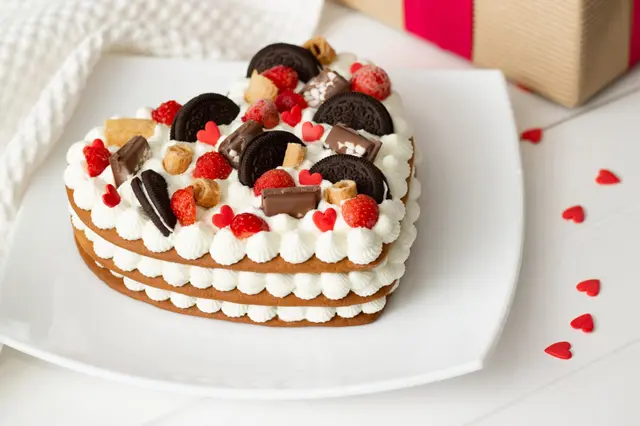 Gâteau en forme de cœur à la ricotta et à la crème fouettée, décoré de chocolat, gaufres, biscuits et fraises