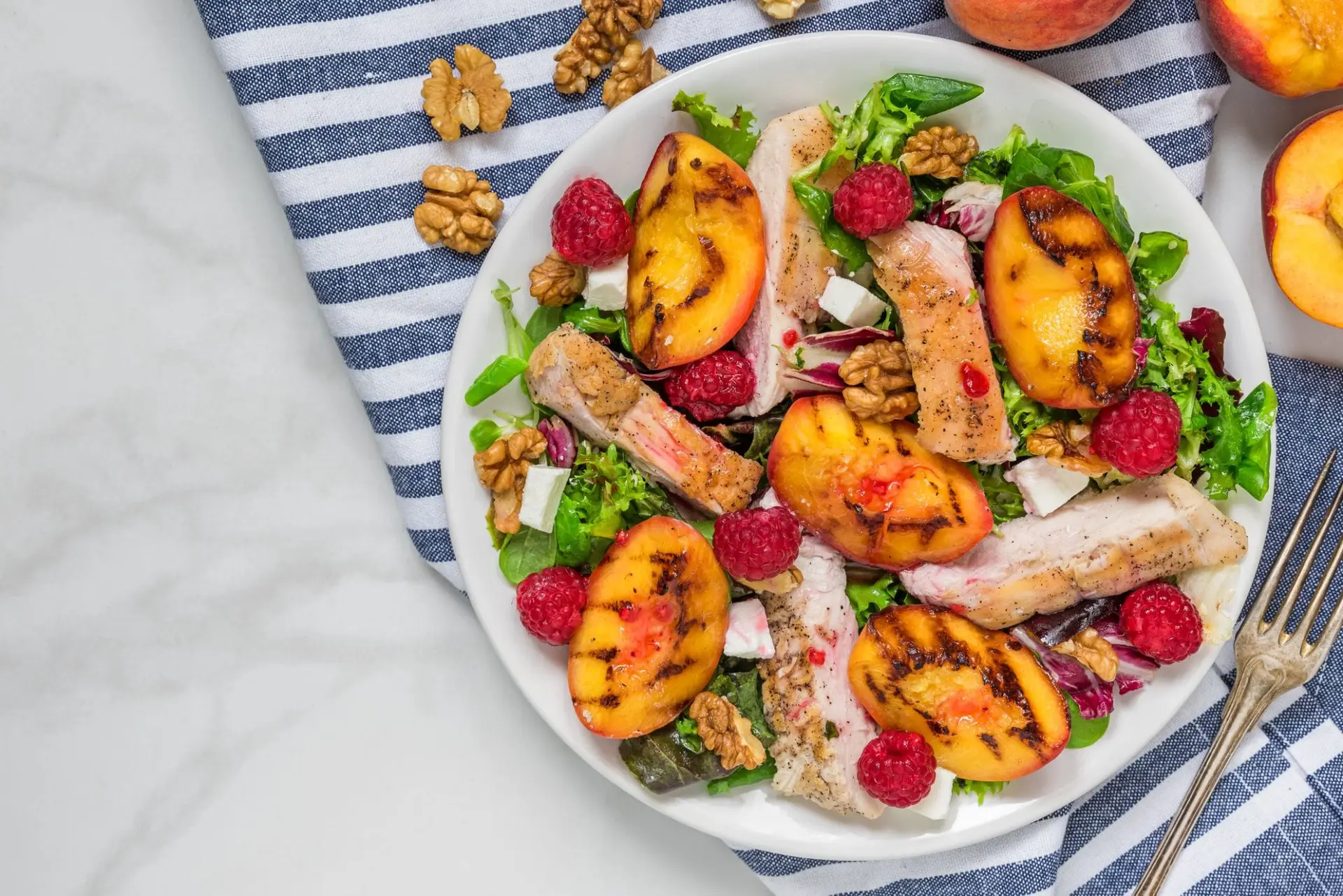 Salade de filet de poulet grillé avec des pêches grillées, des framboises, des noix et du mesclun