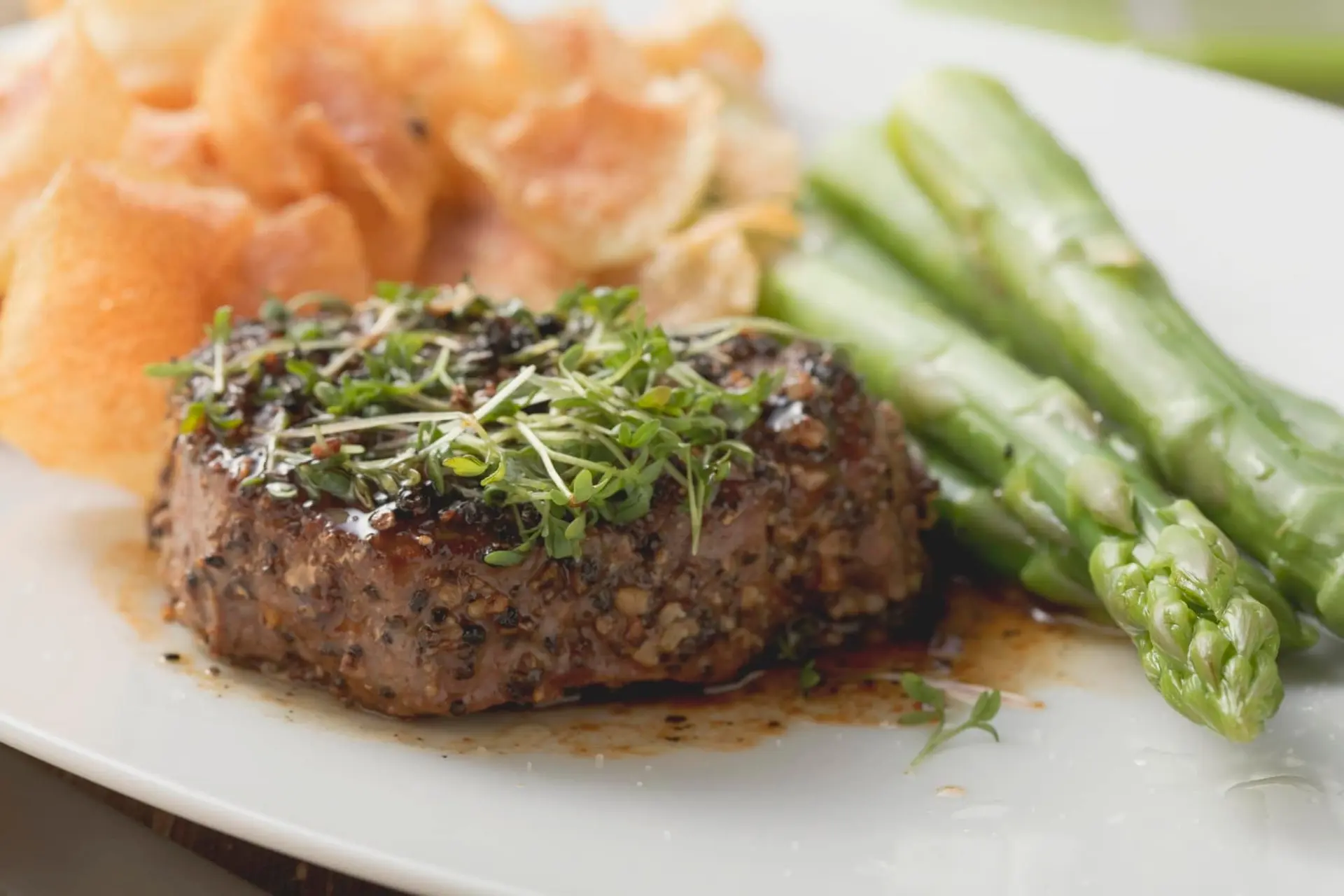 Steak au poivre avec cresson, asperges vertes et chips de pommes de terre