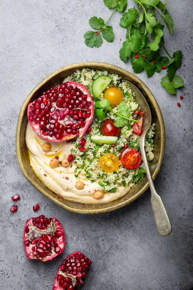 Salade de couscous avec légumes, houmous, grenade et coriandre fraîches