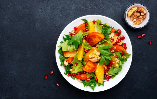 Salade au kaki, aux graines de grenade, noix, tranches d'orange et à la laitue